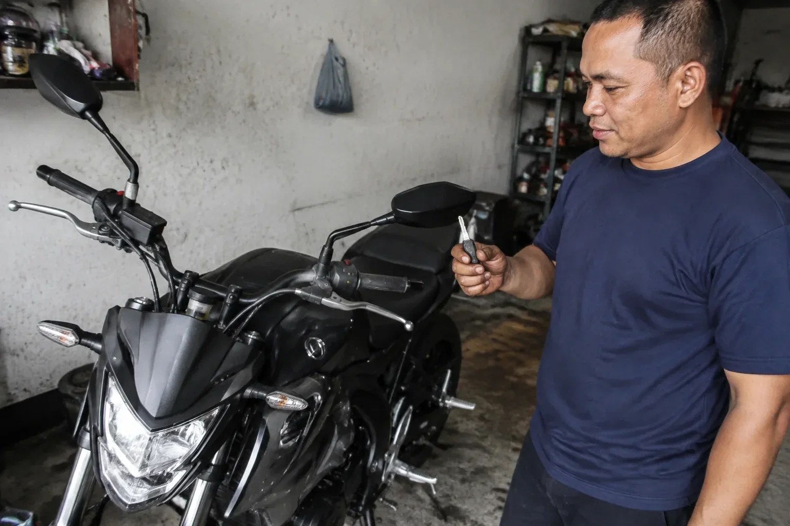 Person holding a key beside a black motorcycle in a garage. — Motorcycle & Scooter Keys, Whitchurch-Stouffville