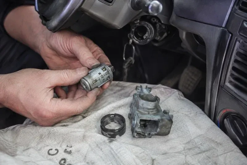 Hands holding a removed ignition cylinder beside a car steering column, with the housing and small parts on a cloth. — Ignition Lock Repair, Whitchurch-Stouffville